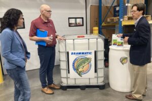 USDA Deputy Secretary Xochitl Torres Small visiting Dramm next to liquid fish fertilizers containers in factory warehouse