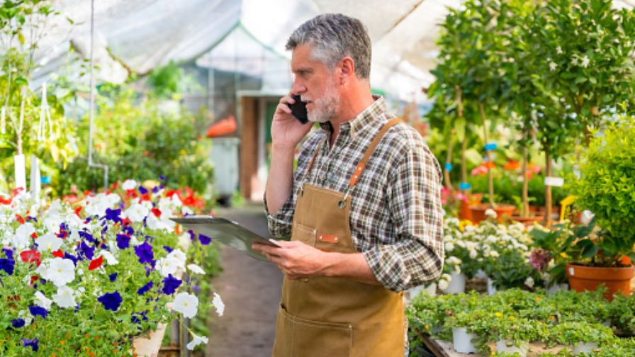 Elderly gardener working in a nursery inside the flower greenhouse making a call, for Hortica Insurance.